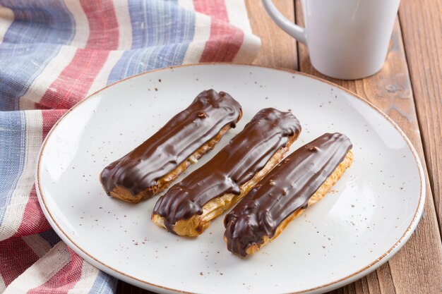 Eclairs al cioccolato sulla zolla bianca sulla tavola di legno