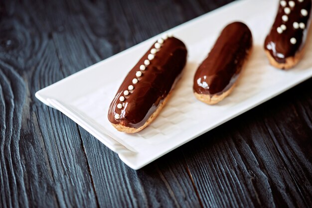 Eclairs con glassa al cioccolato fondente e gocce in un piatto bianco su sfondo scuro