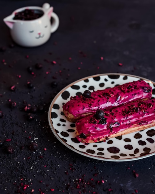 Eclairs da dessert francesi tradizionali con ripieno di frutti di bosco e cioccolato rosa in una composizione su un tavolo scuro e un piatto con punti neri Tazza con ribes nero Spazio per la copia del testo