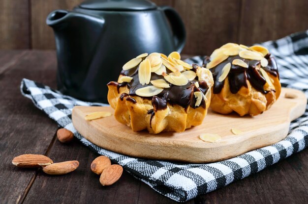 Eclairs, ricoperti di cioccolato fondente e scaglie di mandorle decorative su un tavolo di legno scuro.