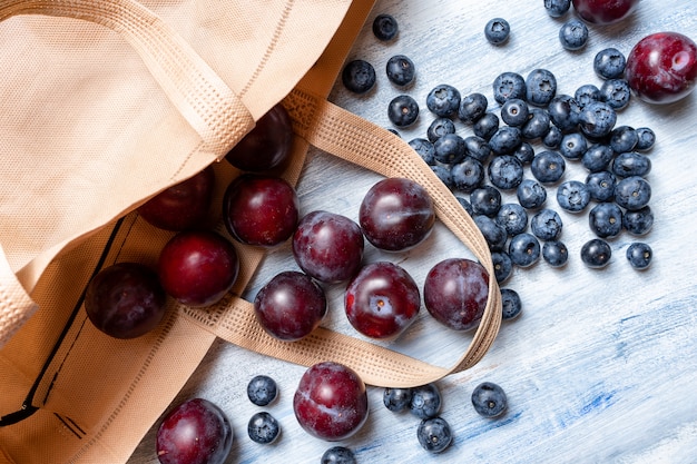 Eco concetto di riciclaggio degli alimenti. bacche diverse (prugna, mirtillo) su una parete di legno blu. Copia spazio. Vista dall'alto. Orizzontale. Borsa in tessuto ecologico. shopping di plastica gratuito. Zero sprechi