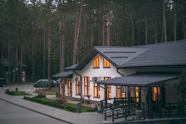 Edificio ristorante bianco con tetto a due falde in pineta, con luci accese in grandi finestre