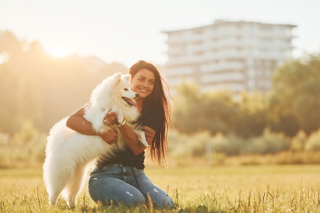 Edificio sullo sfondo Donna con il suo cane si diverte sul campo durante la giornata di sole