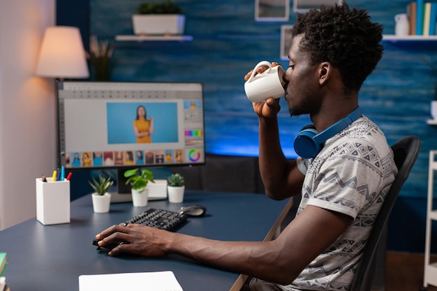 Editor di uomo afroamericano che beve caffè mentre fa il ritocco fotografico