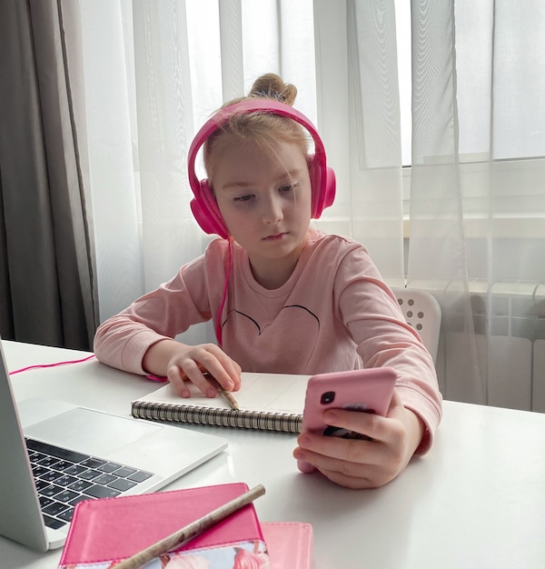 Educazione a distanza. Una studentessa in cuffie rosa che studia i compiti durante la lezione online a casa tramite Internet. Distanza sociale durante la quarantena
