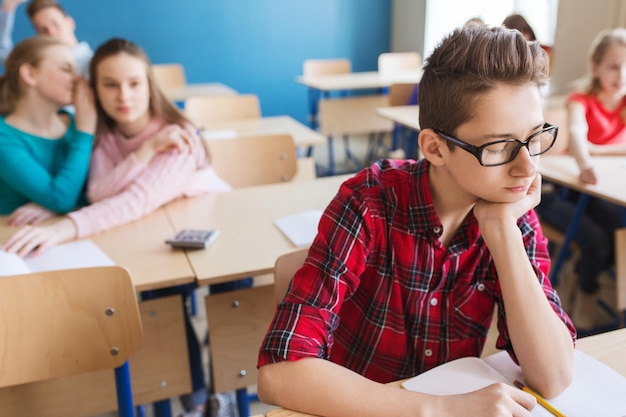 educazione, bullismo, relazioni sociali e concetto di persone - compagni di classe che spettegolano dietro il ragazzo studente a scuola