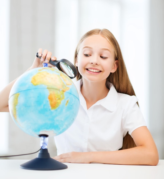 educazione e concetto di scuola - piccola studentessa che guarda il globo con lente d'ingrandimento a scuola