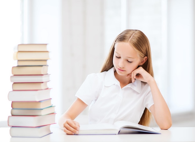 educazione e concetto di scuola - piccola studentessa che studia e legge libri a scuola