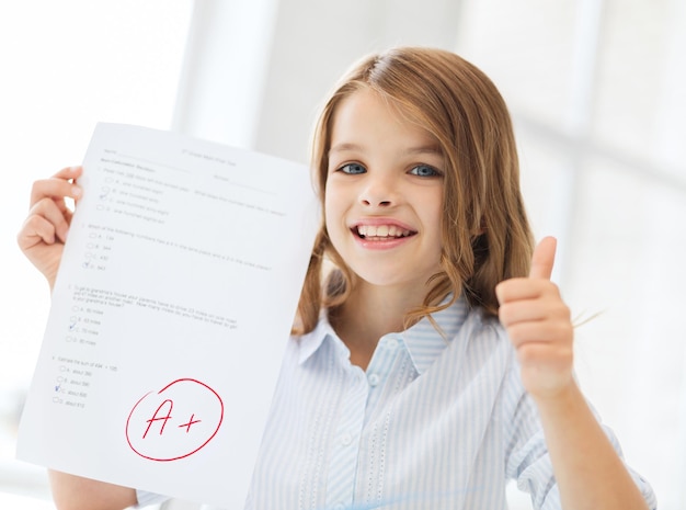 educazione e concetto di scuola - piccola studentessa con test e un voto a scuola che mostra i pollici in su