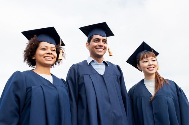 educazione, laurea e concetto di persone - gruppo di studenti internazionali felici in sparvieri e abiti da scapolo all'aperto