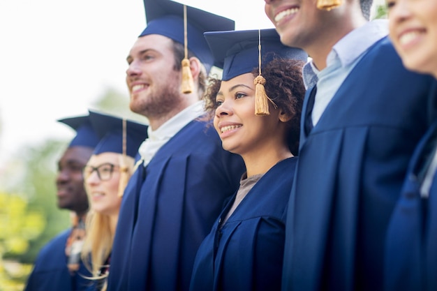 educazione, laurea e concetto di persone - gruppo di studenti internazionali felici in tavole di mortaio e abiti da scapolo all'aperto