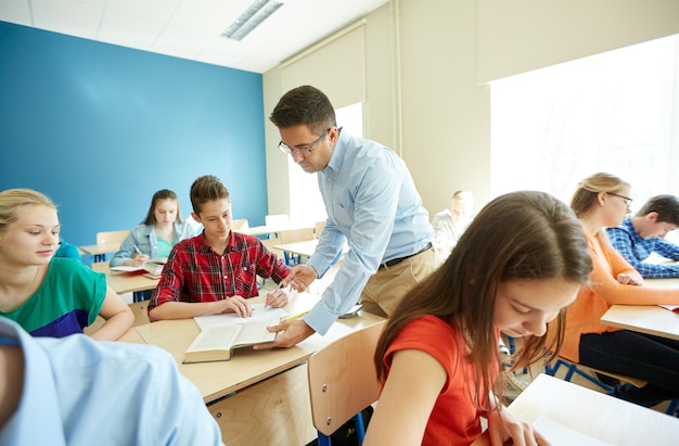 educazione, scuola, apprendimento, insegnamento e concetto di persone - gruppo di studenti con libro e insegnante che aiutano con il compito in classe