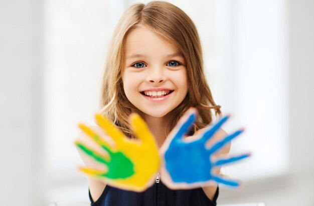 educazione, scuola, arte e concetto di pittura - piccola studentessa che mostra le mani dipinte a scuola