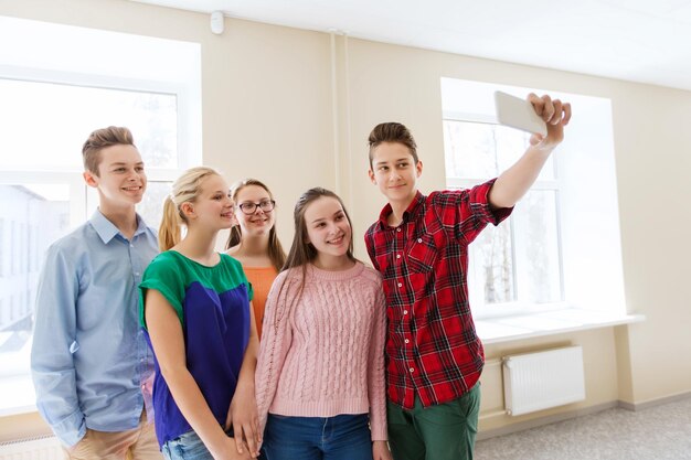 educazione, scuola, tecnologia e concetto di persone - gruppo di studenti sorridenti felici che scattano foto con il selfie stick dello smartphone nel corridoio