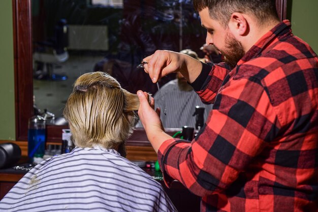 Effetto rinfrescante. il maestro barbiere fa l'acconciatura e lo styling con l'asciugatrice. Concetto Barbershop. uomo hipster con la barba che si taglia i capelli in un negozio di barbiere. Lavoro professionale di parrucchiere. Stile di vita.