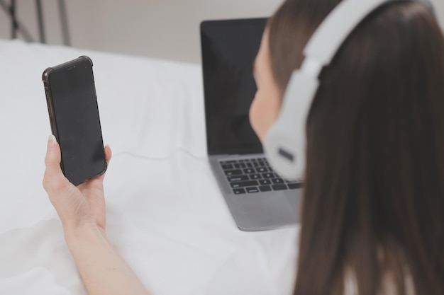 Efficiente giovane ragazza millenaria seduta su un letto al mattino usa il computer portatile e mangia croissant e beve caffè a colazione