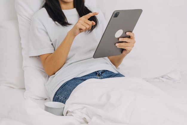 Efficiente giovane ragazza millenaria seduta su un letto al mattino utilizza il computer portatile e mangia croissant e beve caffè per colazione Top Down Shot