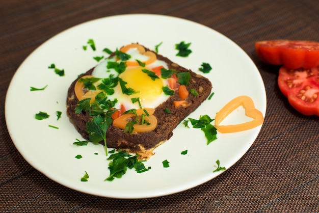 Egg nel pane con le erbe ed i pomodori su un piatto della prima colazione