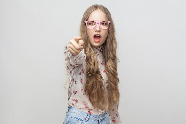 Ei, tu! Ragazza scioccata, puntando il dito verso la telecamera e aprendo la bocca. Studio girato, isolato su sfondo grigio