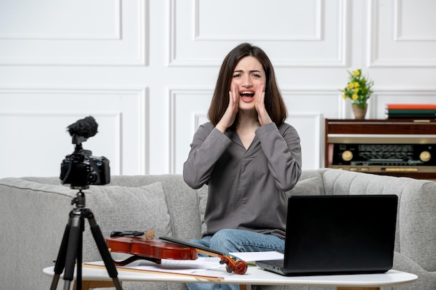 Elearning giovane bella ragazza carina a distanza a casa dando lezioni di violino urlando