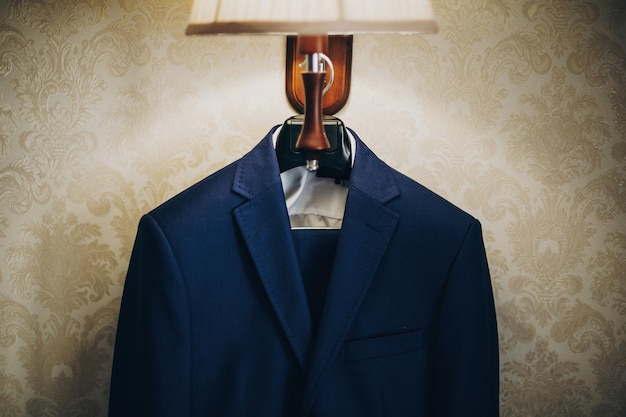 Elegante abito blu per lo sposo appeso alla lampada nella camera d'albergo Preparazione mattutina prima della cerimonia nuziale Abiti per riunioni di lavoro