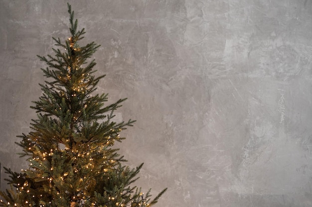 Elegante albero di abete di Natale con luci calde e scintillanti di ghirlanda di fronte a un muro di cemento scuro neutro Celebrazione delle vacanze di Natale e Capodanno