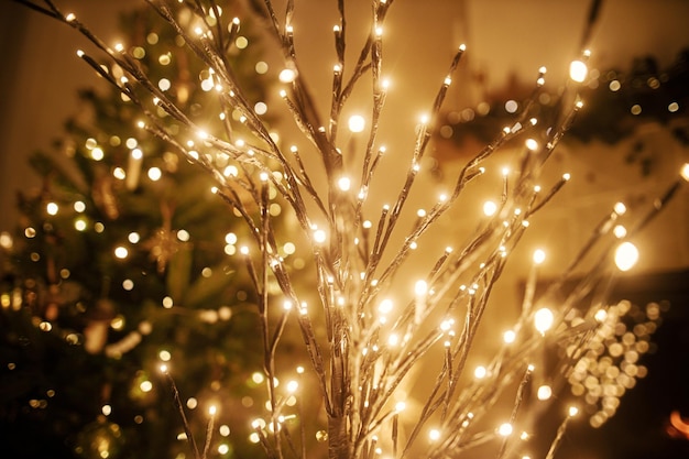 Elegante albero di Natale illuminato su sfondo di luci dorate bokeh albero decorato e caminetto acceso nella sala serale Atmosferica magica vigilia di Natale davanti al caminetto