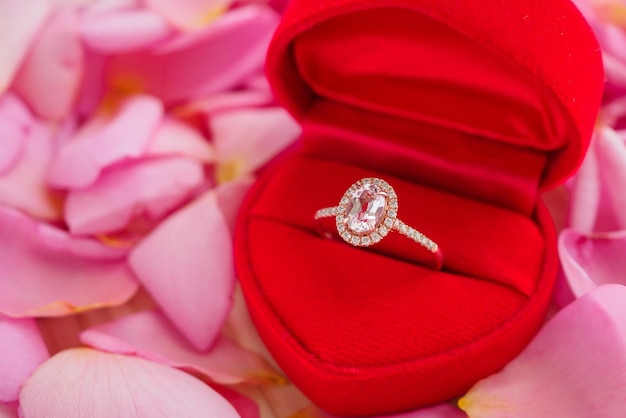 Elegante anello di diamanti da sposa in portagioie a cuore rosso su bellissimo sfondo di petali di rosa rosa