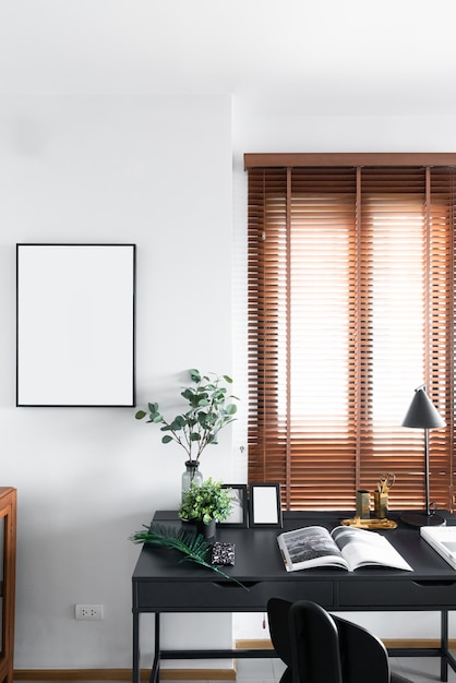 Elegante angolo di lavoro decorato con cornice in legno nero e pianta artificiale in vaso di vetro