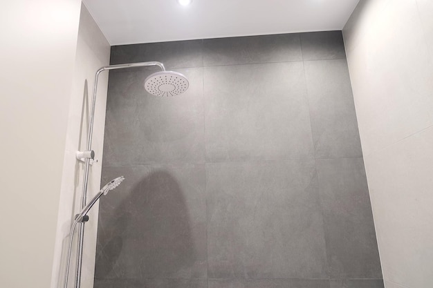 Elegante bagno con grande vasca da bagno, piastrelle grigie, armadio in legno e doccia. Interno moderno del bagno con illuminazione minimalista e toilette illuminata