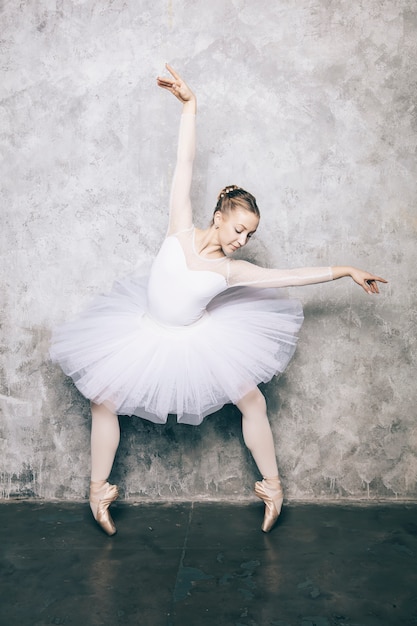 Elegante ballerina in abito bianco danza contro il muro rustico