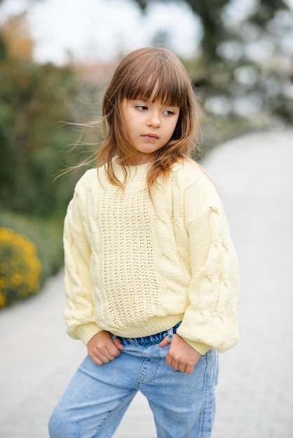 Elegante bambina di 5-6 anni indossa un maglione casual alla moda e pantaloni di jeans che camminano nel parco all'aperto. Primavera. Bambino sopra la priorità bassa della sorgente della natura. Infanzia.