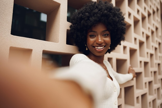 Elegante bella donna africana con acconciatura afro in posa vicino al muro geometrico