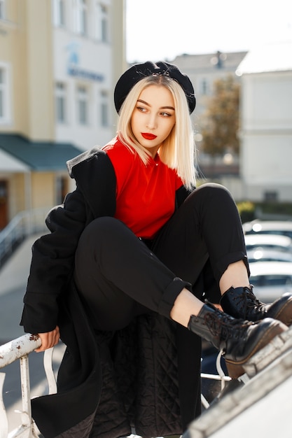 Elegante bella donna bionda in un cappotto nero autunno alla moda con un berretto all'aperto in una giornata di sole