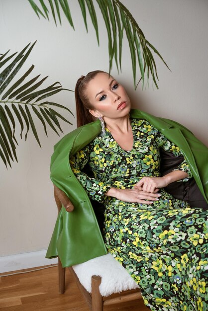 Elegante bella donna in giacca di pelle verde e abito colorato seduto su una sedia in posa su un...