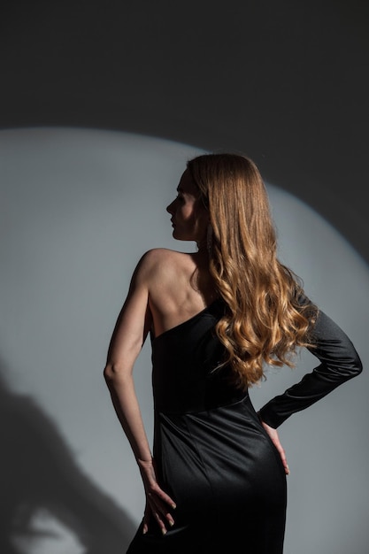 Elegante bella giovane donna in un abito da sera di moda nero su uno sfondo scuro alla vista posteriore del partito