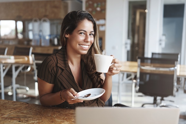 Elegante bella signora dell'ufficio che gode della tazza calda della tenuta del caffè sitttin nel caffè da solo