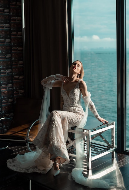 Elegante bella sposa con lunghi capelli castani ondulati che indossa un abito da sposa bianco con vista sul mare