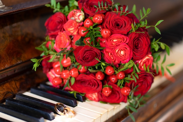 Elegante bouquet da sposa di rose rosse al pianoforte. Dettagli del matrimonio.