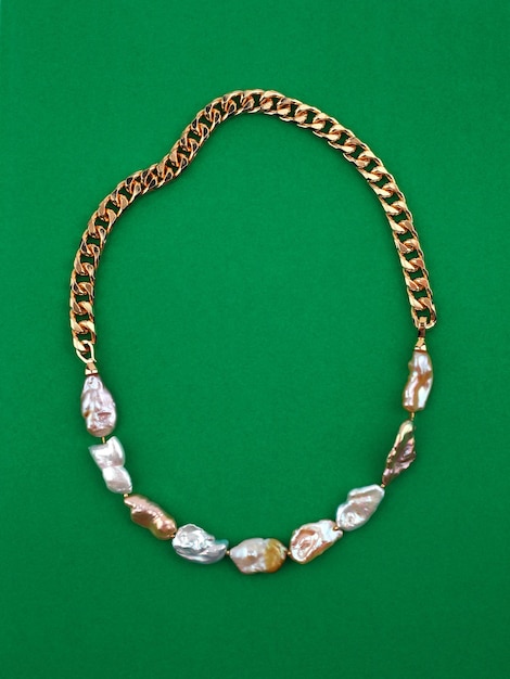 Elegante collana di perle barocche a catena dorata di lusso su sfondo verde Colpo del primo piano