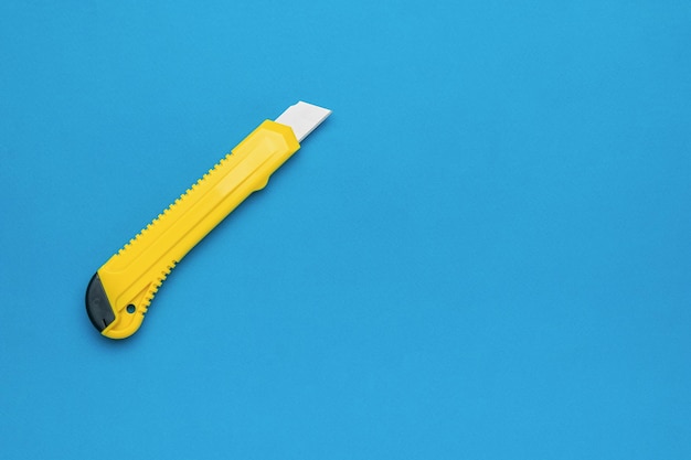 Elegante coltello da cancelleria giallo su sfondo blu brillante Concetto minimalista