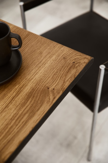 Elegante composizione di tavolo artigianale in legno con sedie nere di design, tazza e pavimento in cemento.