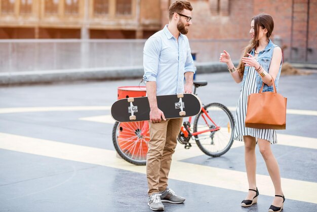 Elegante coppia d'affari in piedi insieme a skateboard e bicicletta all'aperto nel parco giochi sul tetto