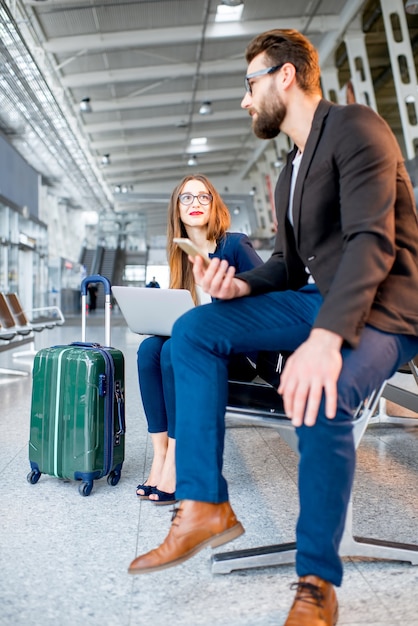 Elegante coppia d'affari seduta con laptop e bagagli nella sala d'attesa dell'aeroporto. Avere una conversazione di lavoro durante il viaggio in aeroporto