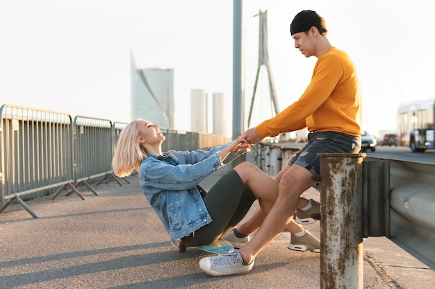 Elegante coppia di adolescenti con un longboard sul ponte durante il tramonto