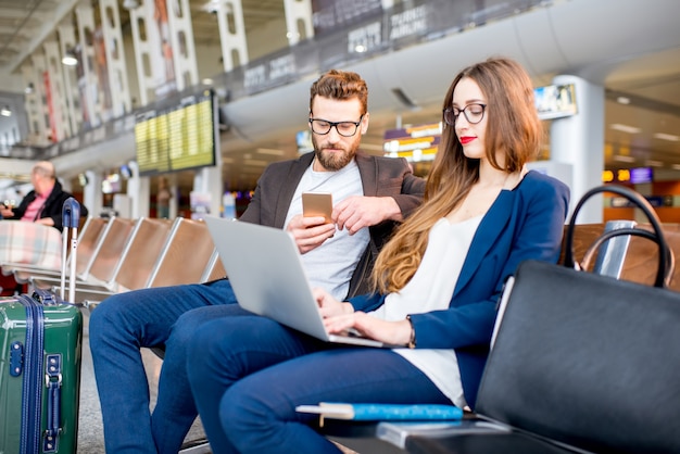 Elegante coppia di affari che lavora con laptop e telefono seduti nella sala d'attesa dell'aeroporto. Concetto di viaggio d'affari