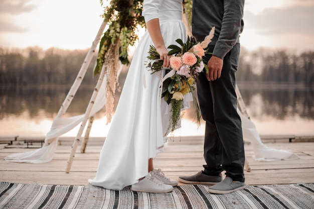 Elegante coppia di sposi in scarpe sportive e abiti da sposa sulla riva del fiume