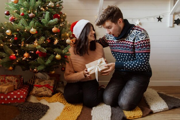 Elegante coppia emotiva che si scambia regali di Natale sotto l'albero di Natale nella sala festiva