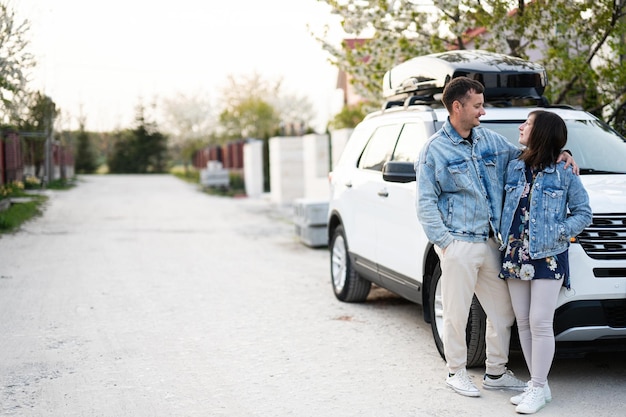 Elegante coppia in giacca di jeans in piedi vicino a un'auto suv americana bianca con portapacchi