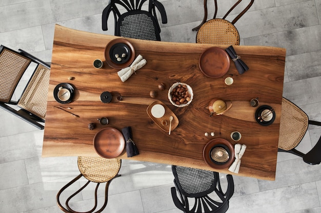 Elegante design degli interni della sala da pranzo con tavolo in legno di noce, sedie retrò, stoviglie, piatti, tovaglia, teiera, cibo, decorazioni e accessori eleganti. Pavimento in cemento. Vista dall'alto.